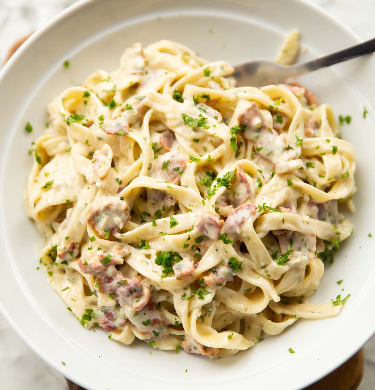 close up shot of creamy bacon pasta in large white dish with silver fork