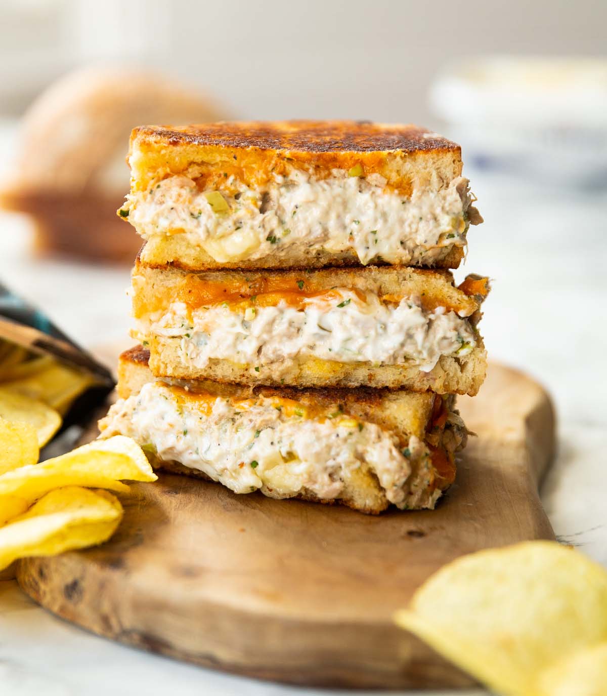 3 tuna melt halves stacked on each other on wooden chopping board with crisps